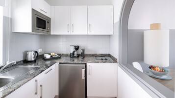 Una cocina compacta con armarios blancos, un refrigerador de acero inoxidable, un microondas y una cafetera.