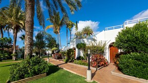 Un jardín bien cuidado con palmeras y un sendero que conduce a un edificio blanco con una puerta de madera.