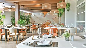 Un restaurante moderno con varias mesas, sillas color naranja y lámparas de mimbre colgantes.