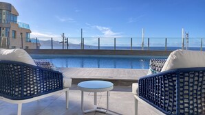 A rooftop pool area with two wicker chairs and a small table, overlooking a clear blue sky and a distant view of mountains.