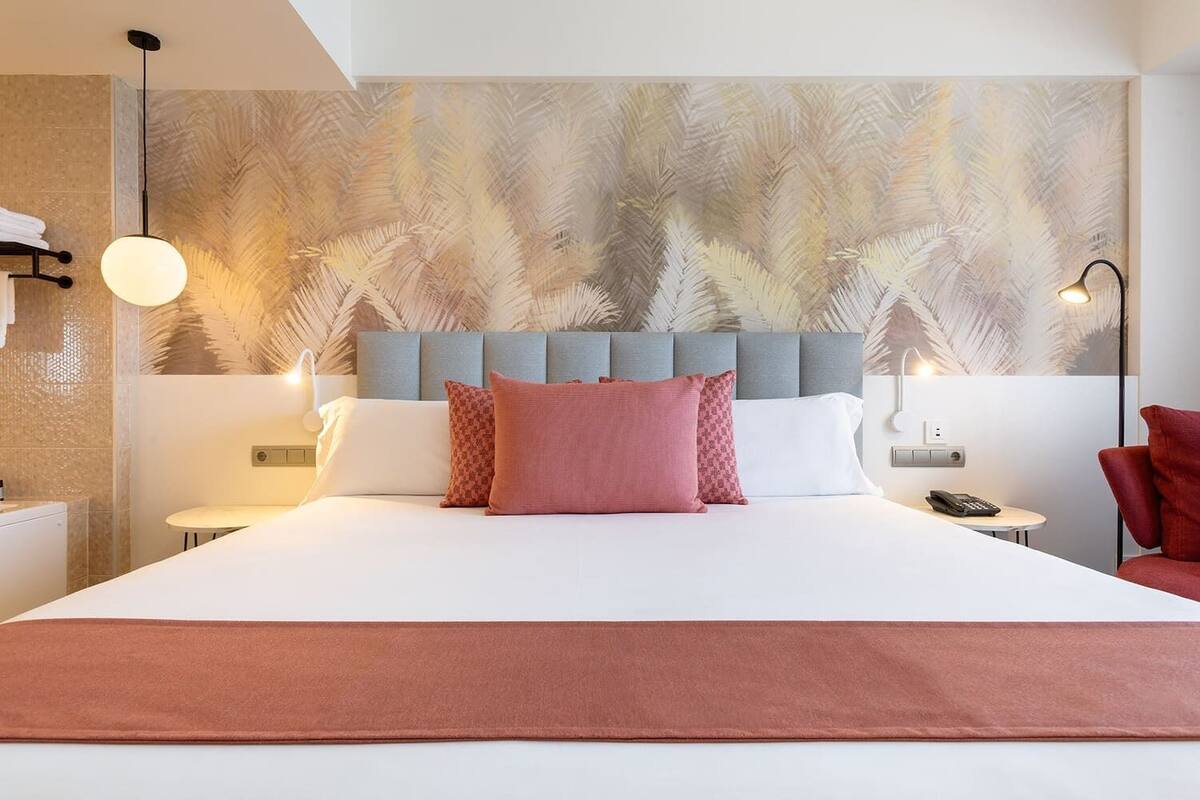 A hotel room with a large bed, a headboard with a leaf pattern, two bedside tables with lamps, and a red chair.