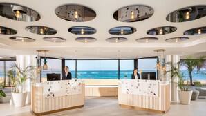 A reception area with a view of the ocean, featuring a modern design with circular ceiling lights and a large window.