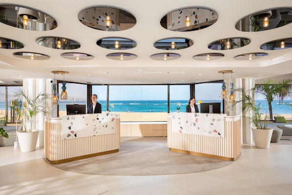 A reception area with a view of the ocean, featuring a modern design with circular ceiling lights and a large window.