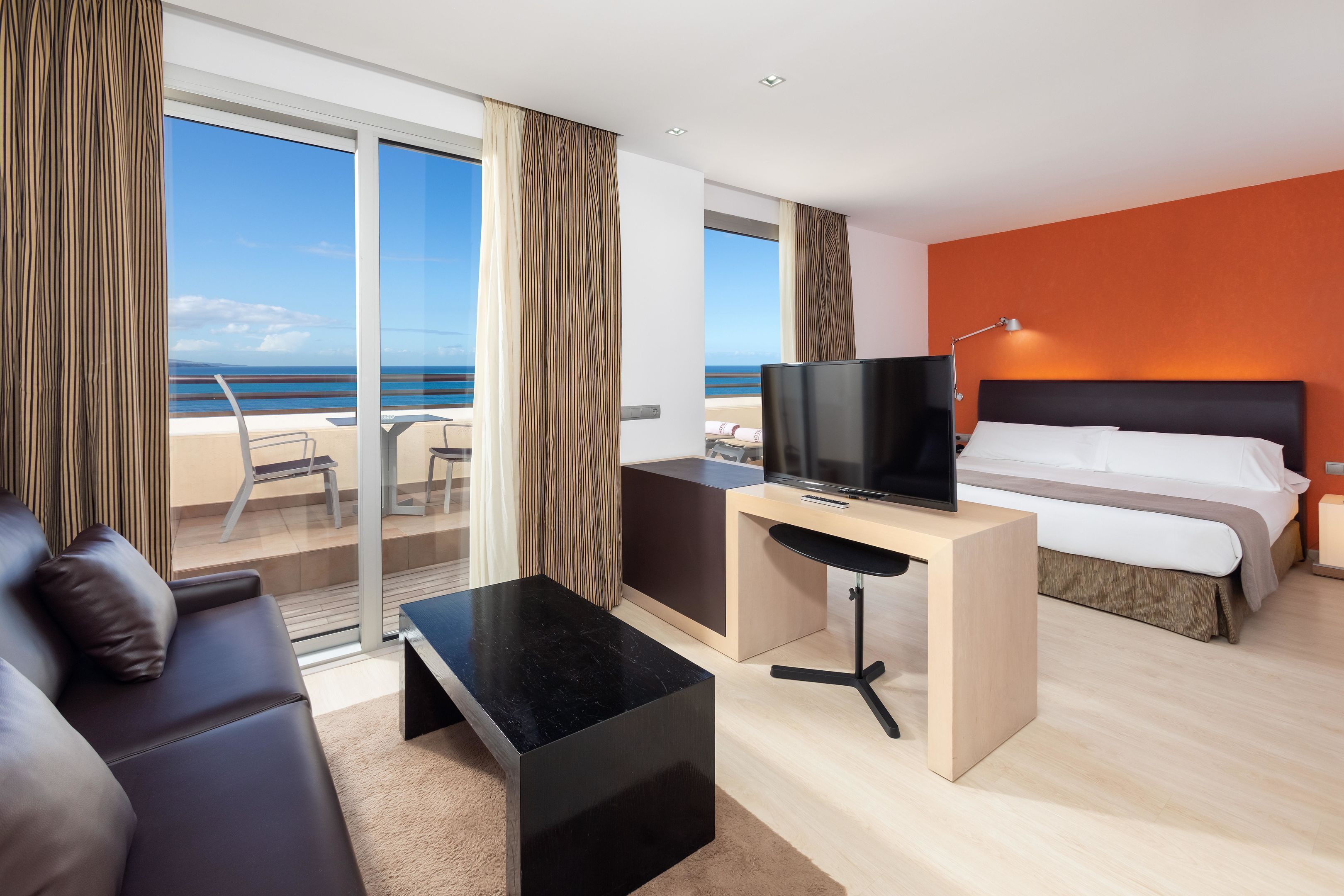 Una habitación de hotel moderna con balcón, cama, escritorio y televisor.