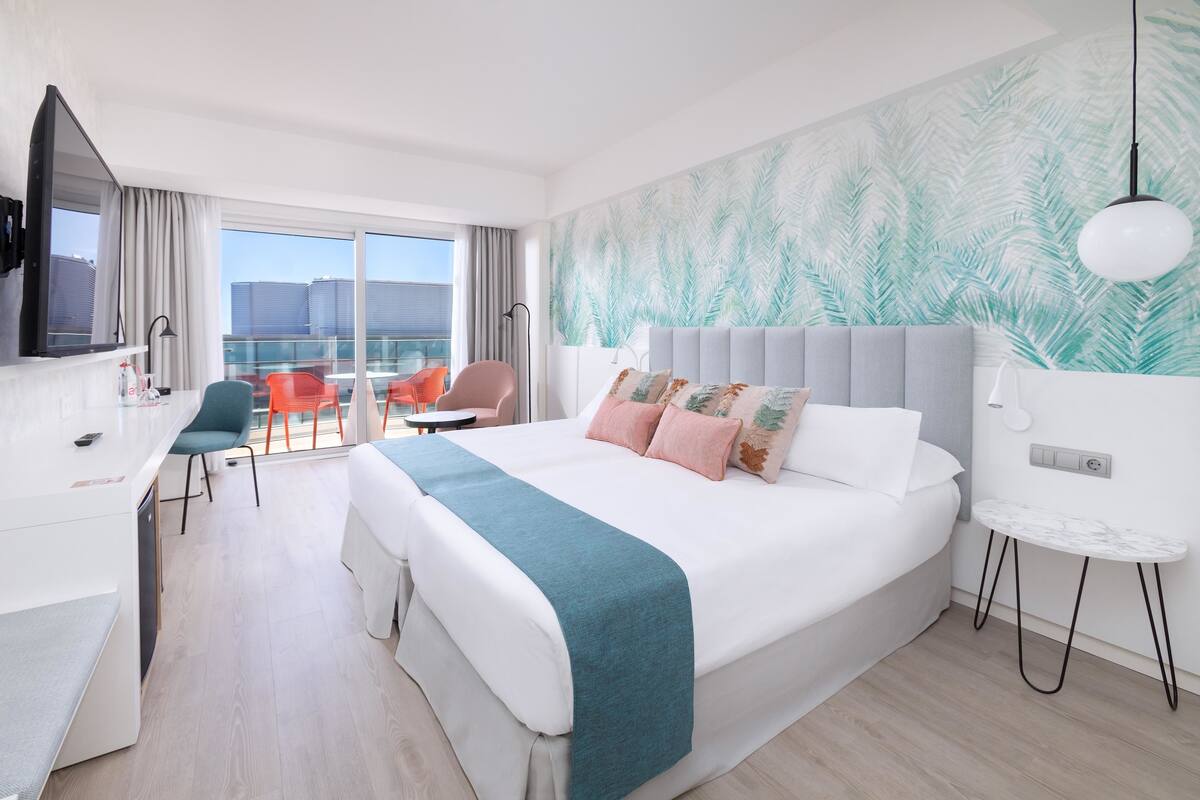 A modern hotel room with a large bed, a desk, a chair, and a view of the city.