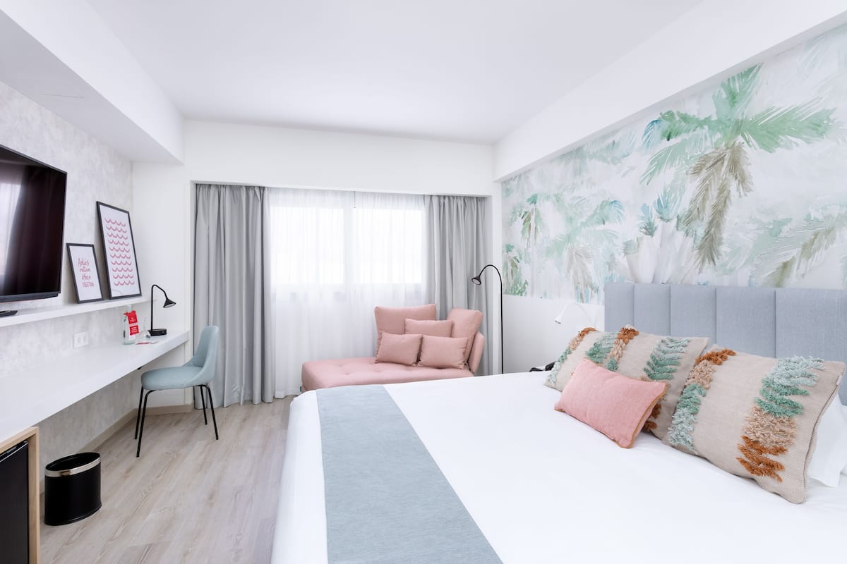 A modern hotel room with a bed, a desk, a chair, and a TV.