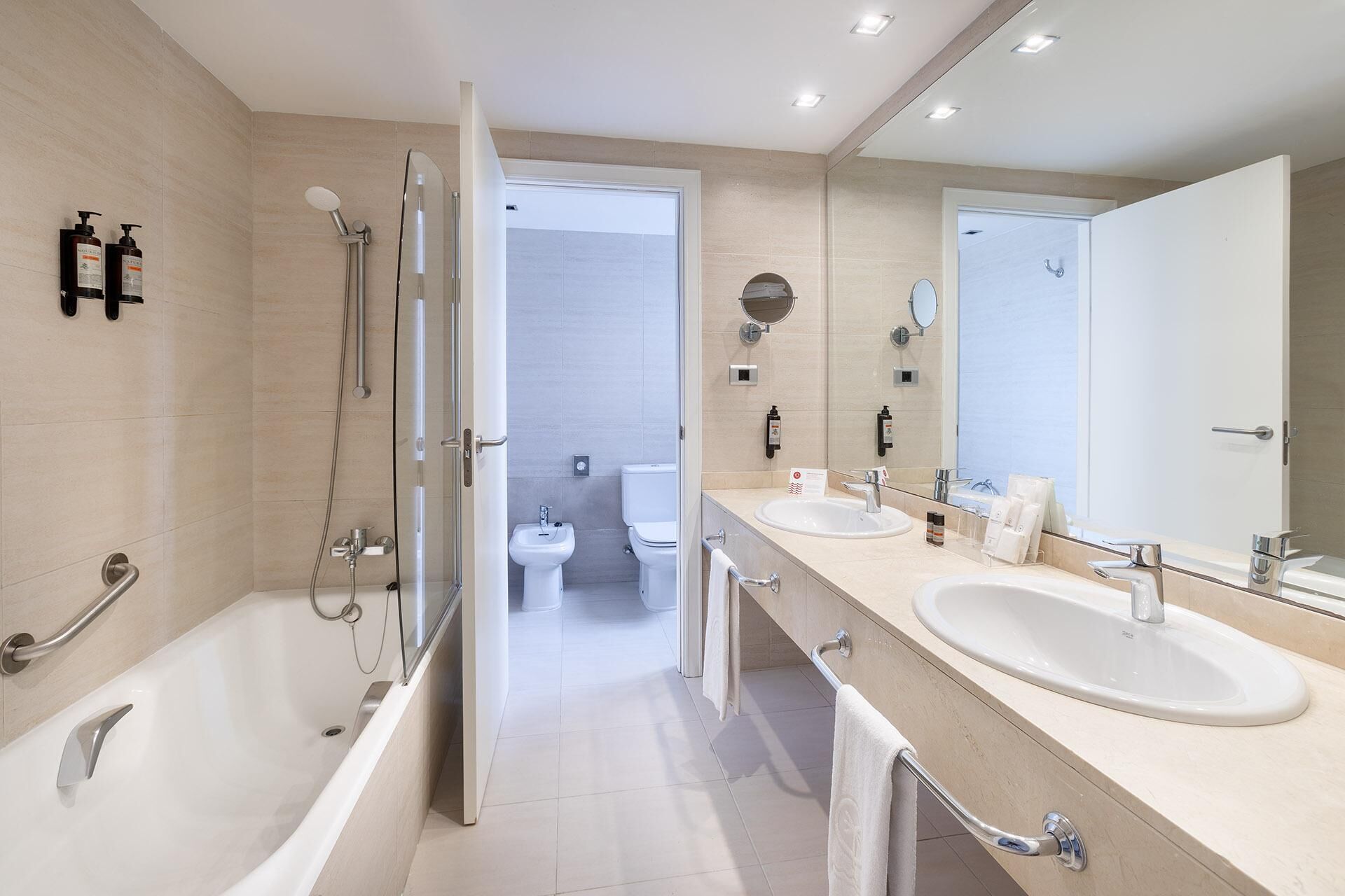 Un baño moderno con bañera, dos lavamanos, inodoro y zona de ducha.