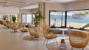 A spacious lobby with wicker chairs, a round table, and large windows offering a view of the beach.