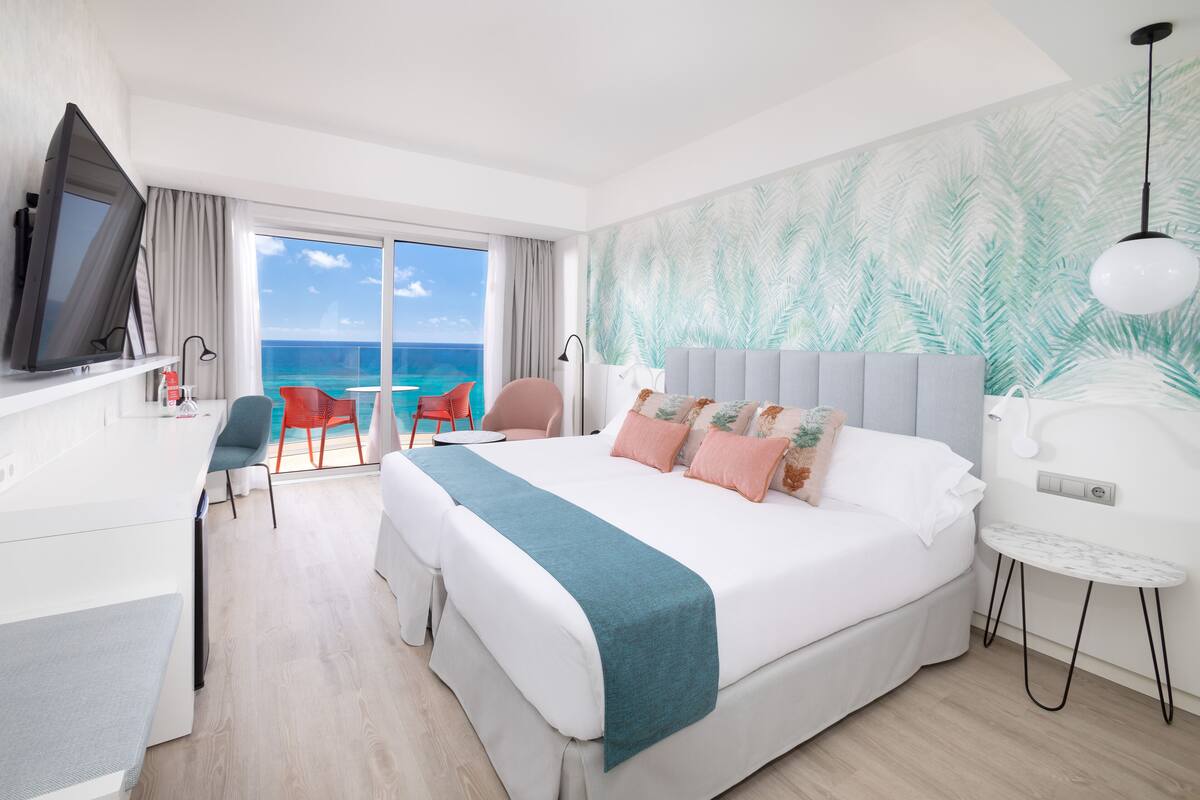 A modern hotel room with a large bed, a desk, and a view of the ocean.