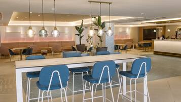 A modern hotel lobby with a long reception desk, blue bar stools, and hanging pendant lights.