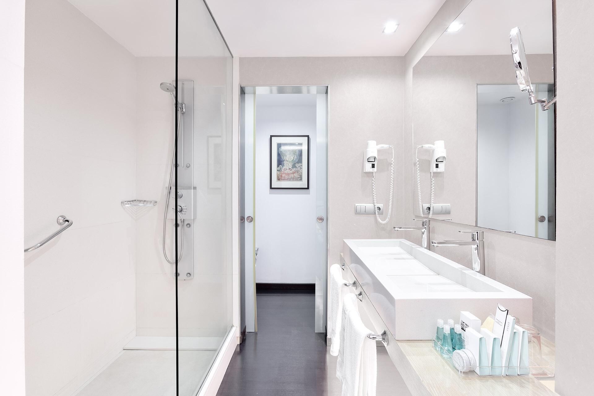 Un baño moderno con cabina de ducha de vidrio, un espejo grande y tocador con artículos de aseo.