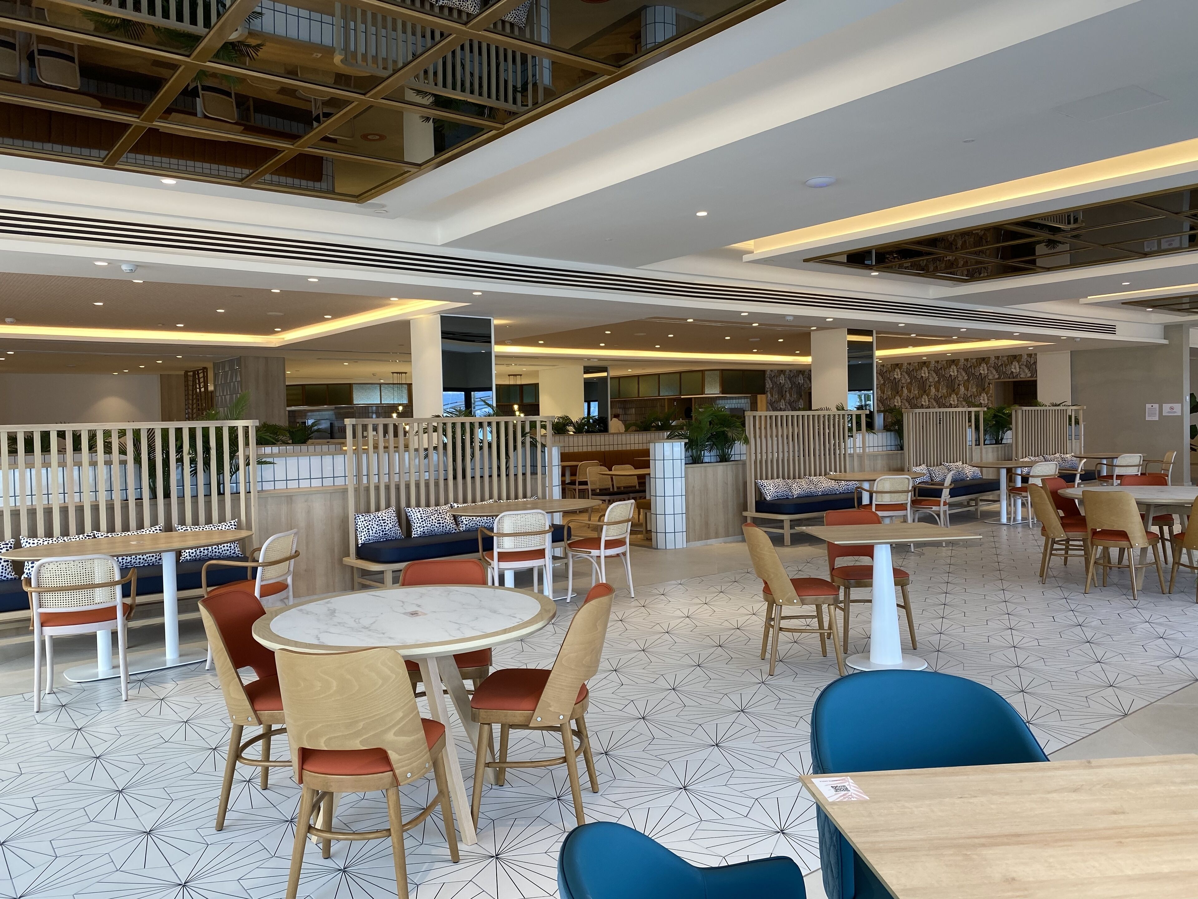 Un amplio comedor interior con diversas opciones de asientos, incluyendo mesas redondas y cabinas, y un techo alto con estructura en forma de cuadrícula.
