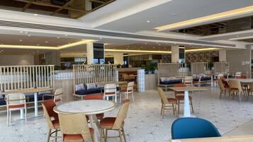 Un amplio comedor interior con diversas opciones de asientos, incluyendo mesas redondas y cabinas, y un techo alto con estructura en forma de cuadrícula.