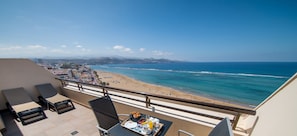 A balcony with a table set for breakfast, overlooking a beach with a clear view of the ocean and distant mountains.