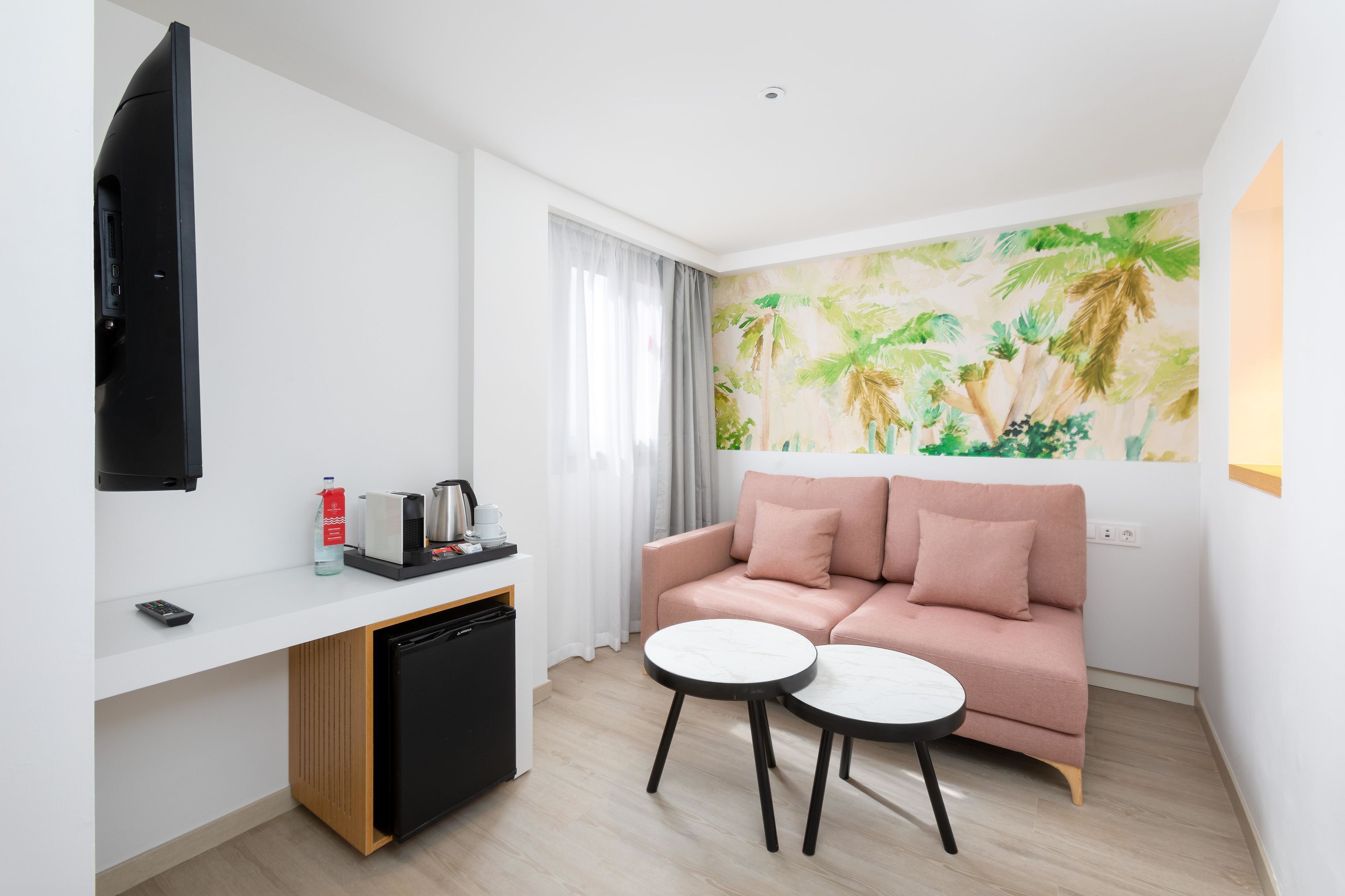 Une chambre d’hôtel moderne équipée d’un canapé, de deux petites tables rondes, d’une machine à café et d’un téléviseur fixé au mur.