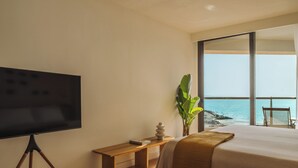 A bedroom with a large bed, a television on a tripod stand, a small table, a plant, and a view of the ocean. - Paradisus by Meliá Fuerteventura – All Inclusive (Pajara)