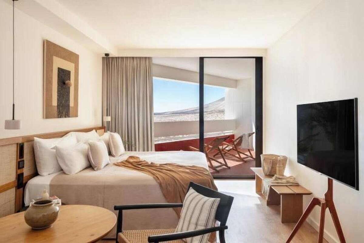 A hotel room with a bed, a TV, a table, and a view of the outdoors.