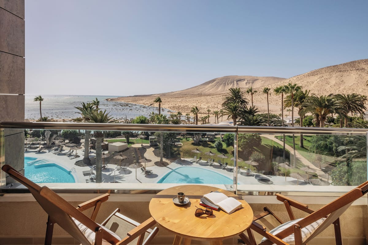 A balcony with a view of a pool, palm trees, and a desert landscape.