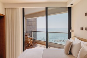 Hotelkamer met een groot bed, een balkon met uitzicht op het strand, een zithoek met een tafel en stoelen, en een groot raam.