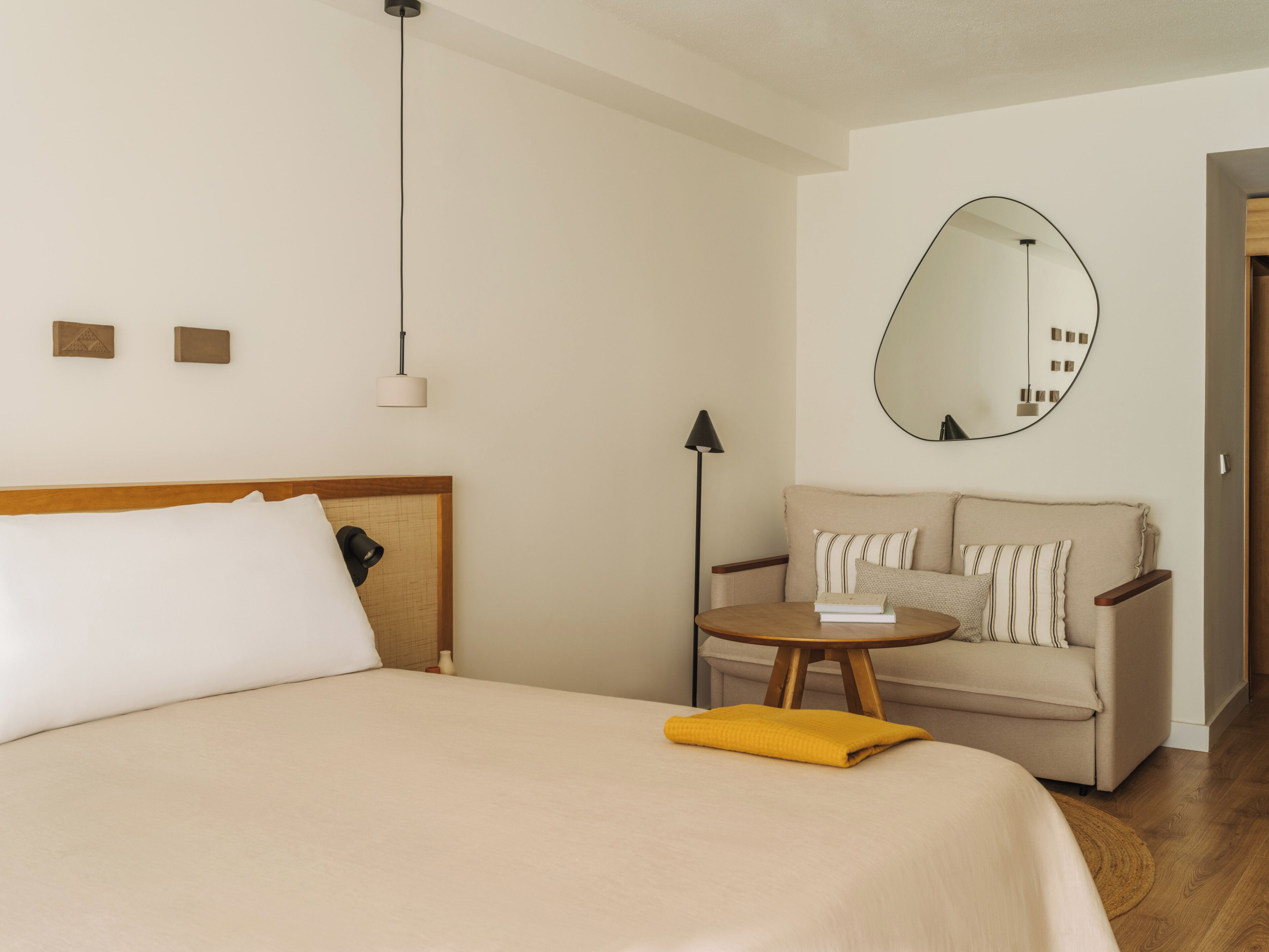 Una habitación de hotel con cama, sofá, una mesita, lámpara, espejo y suelo de madera.