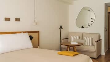 Una habitación de hotel con cama, sofá, una mesita, lámpara, espejo y suelo de madera.