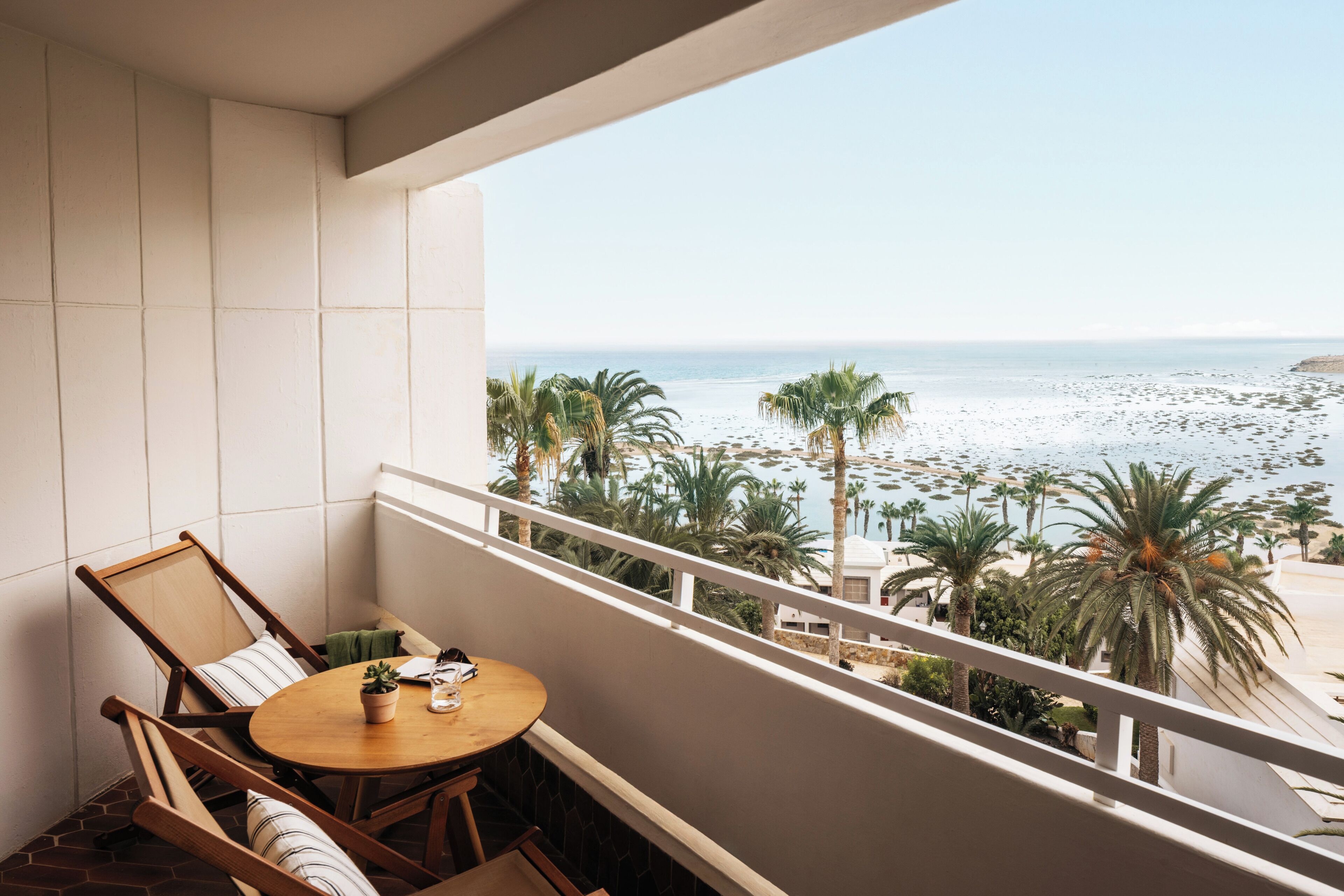 A balcony with a view of the beach and palm trees.