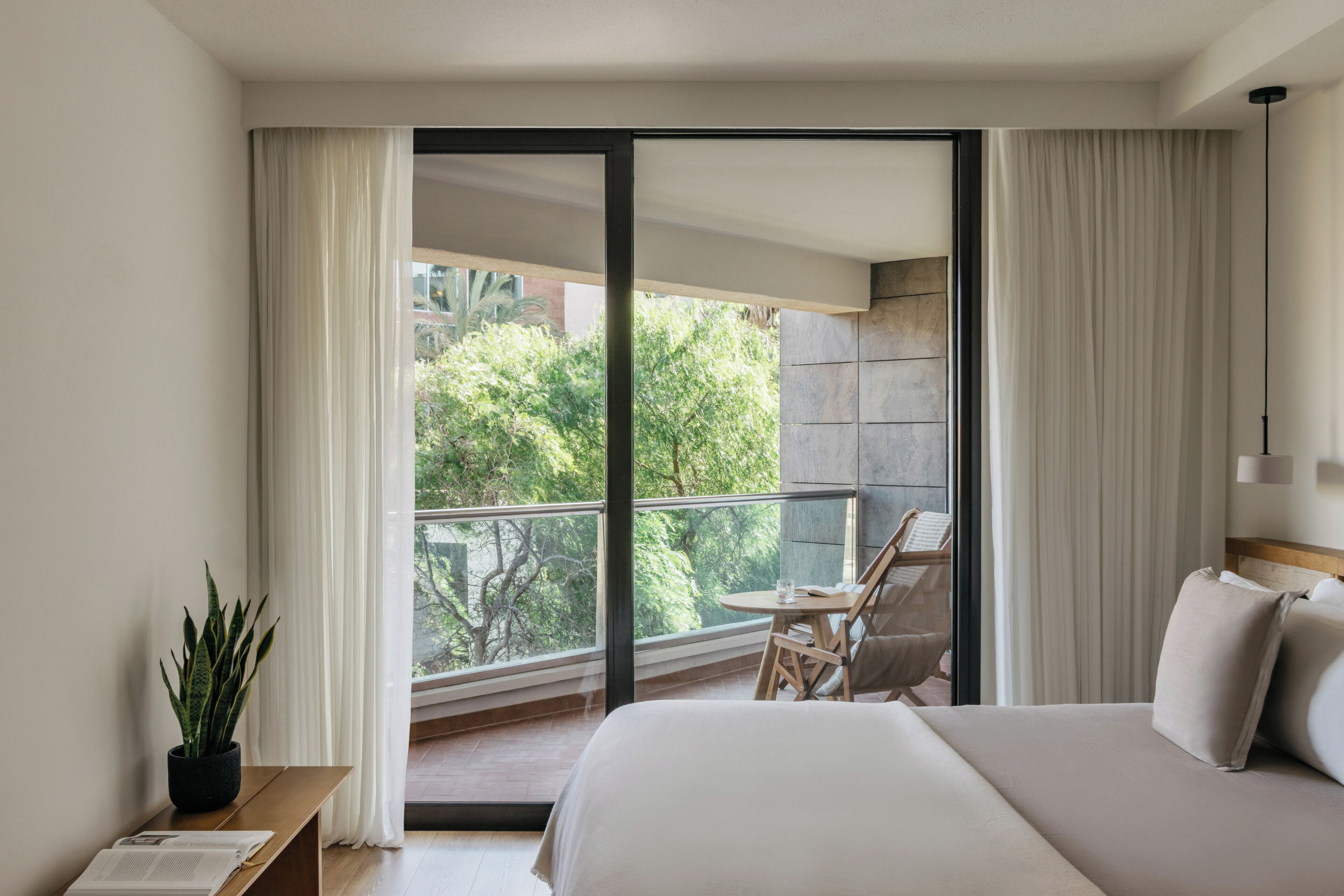 Habitación de hotel moderna con una cama grande, una mesita, una silla y un balcón con vistas a zonas verdes.