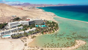 An aerial view of a coastal resort with multiple hotel buildings, a large swimming pool, and a beach with clear turquoise waters. - Paradisus by Meliá Fuerteventura – All Inclusive (Pajara)