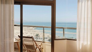 A room with a large window overlooking a beach, a wooden chair, and a table with a book. - Paradisus by Meliá Fuerteventura – All Inclusive (Pajara)
