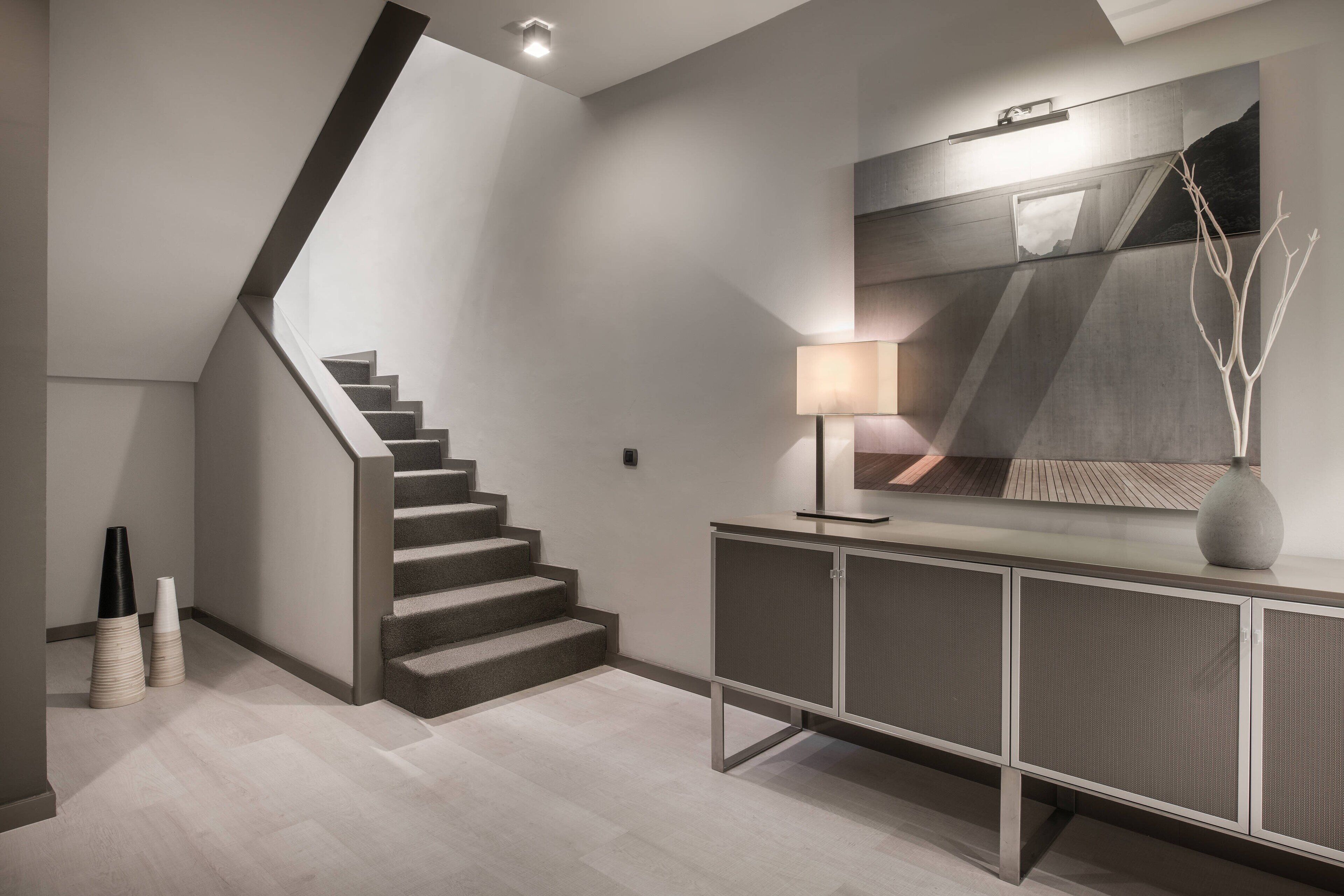 A modern staircase with a minimalist design, a console table with a lamp, and a decorative vase.