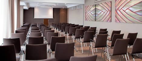 A conference room with rows of chairs, a projector screen, and abstract wall art.