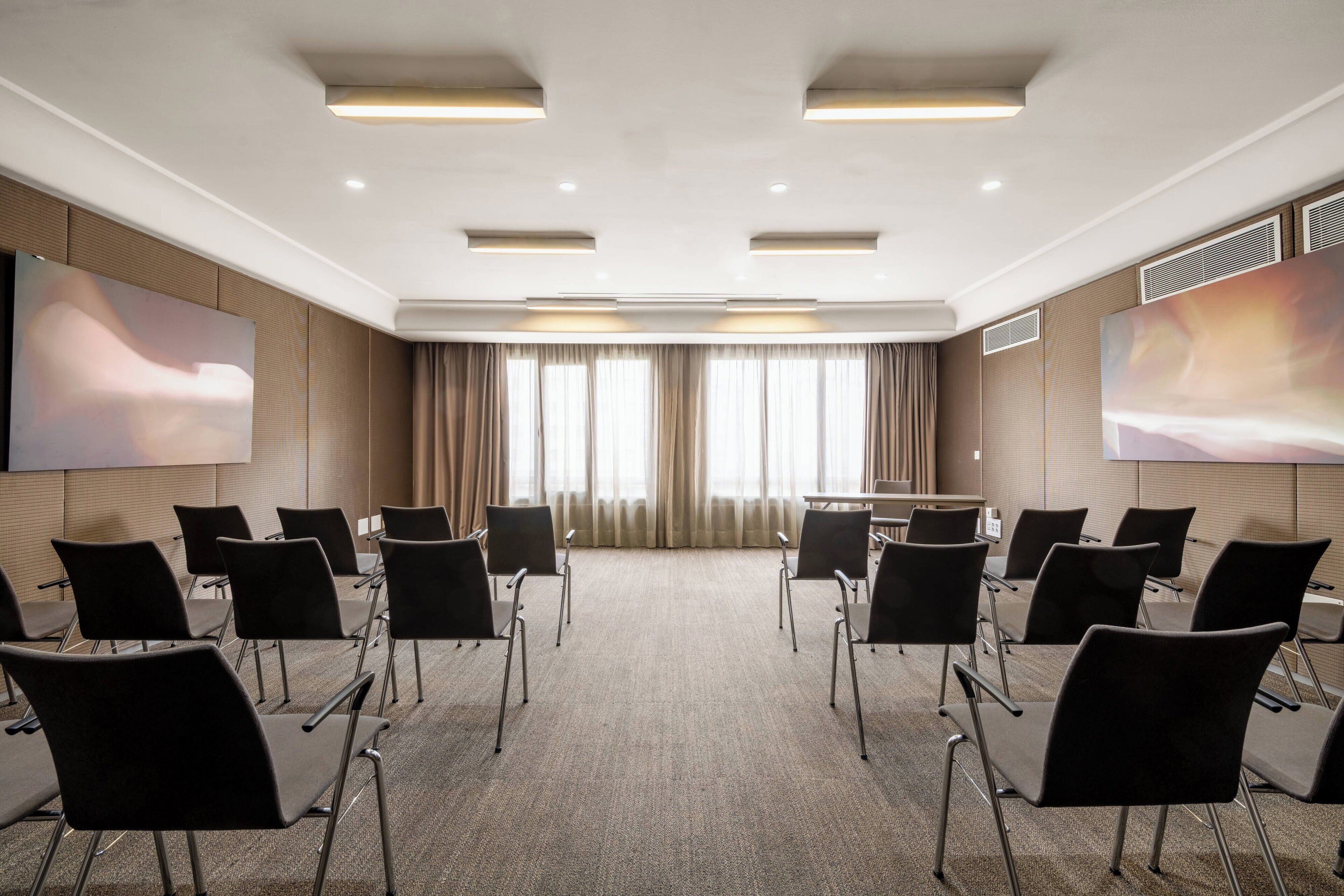 Una sala de conferencias con piso alfombrado, sillas negras, una mesa grande y dos pantallas grandes fijadas a la pared.