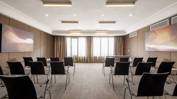 Una sala de conferencias con piso alfombrado, sillas negras, una mesa grande y dos pantallas grandes fijadas a la pared.