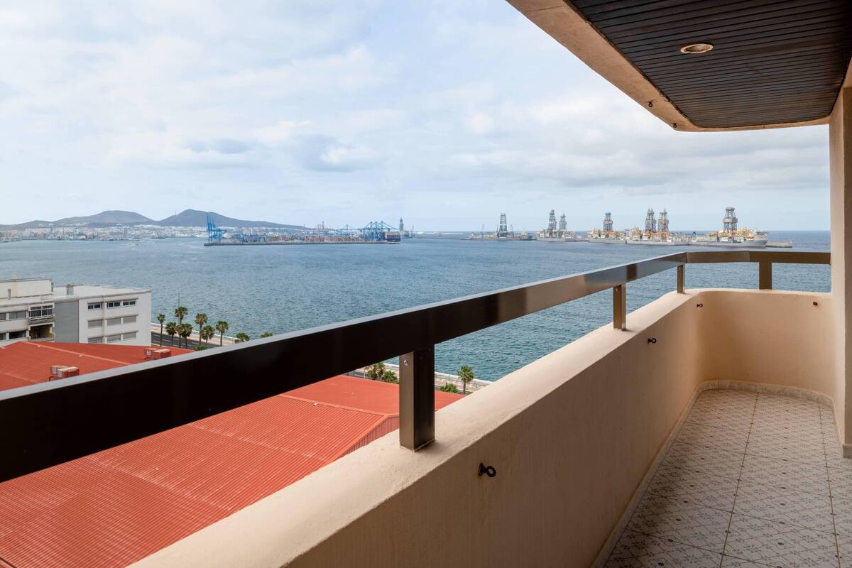 Ein Balkon mit Blick auf das Meer, Industriegebäude und ein ferner Berg.