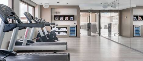 A modern gym with multiple treadmills, a reception area, and a view of the outside through large windows.