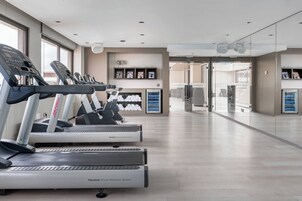 Un gimnasio moderno con cintas de correr, una zona de recepción y vistas al exterior a través de amplios ventanales.
