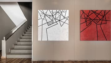 Un escalier menant à un palier où sont accrochées deux peintures abstraites au mur.