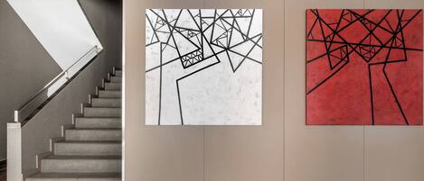 Una escalera que lleva a un rellano con dos cuadros abstractos en la pared.