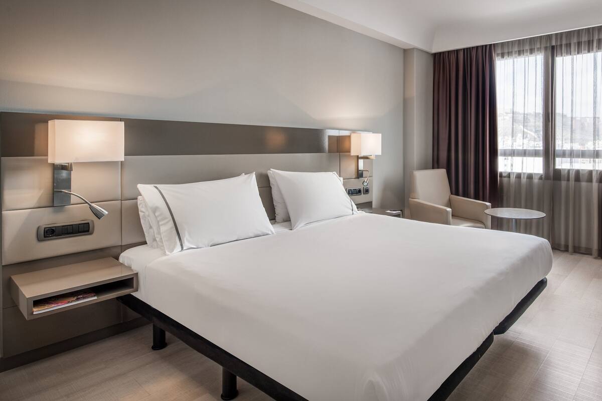 Une chambre d’hôtel moderne avec un grand lit, des tables de chevet, une chaise et une petite table.