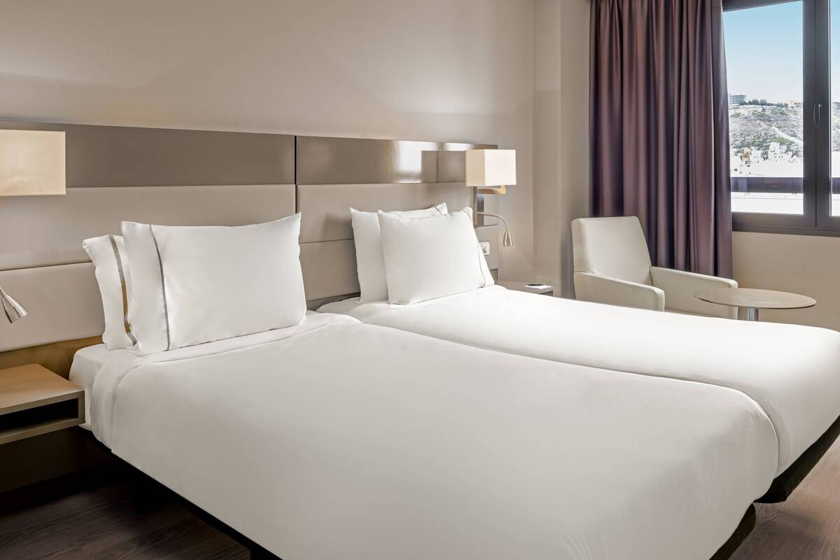 Une chambre d’hôtel avec deux lits, un bureau, une chaise et une petite table.