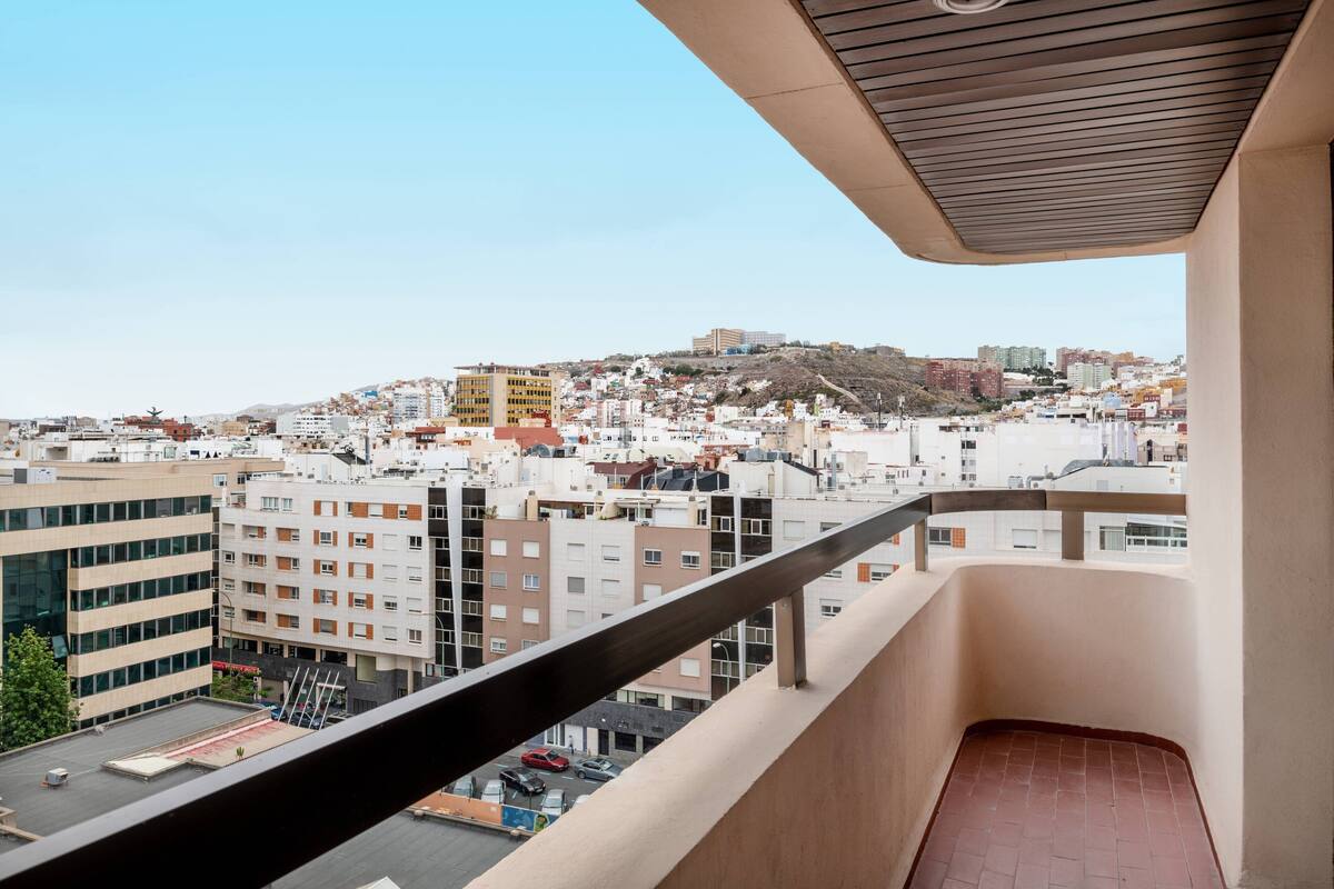 Un balcon offrant une vue sur le paysage urbain, avec des bâtiments et une colline visible au loin.