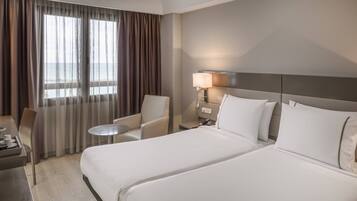 Une chambre d’hôtel avec un grand lit, un bureau avec une chaise, une petite table ronde et une lampe.