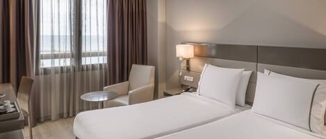 A hotel room with a large bed, a desk with a chair, a small round table, and a lamp.