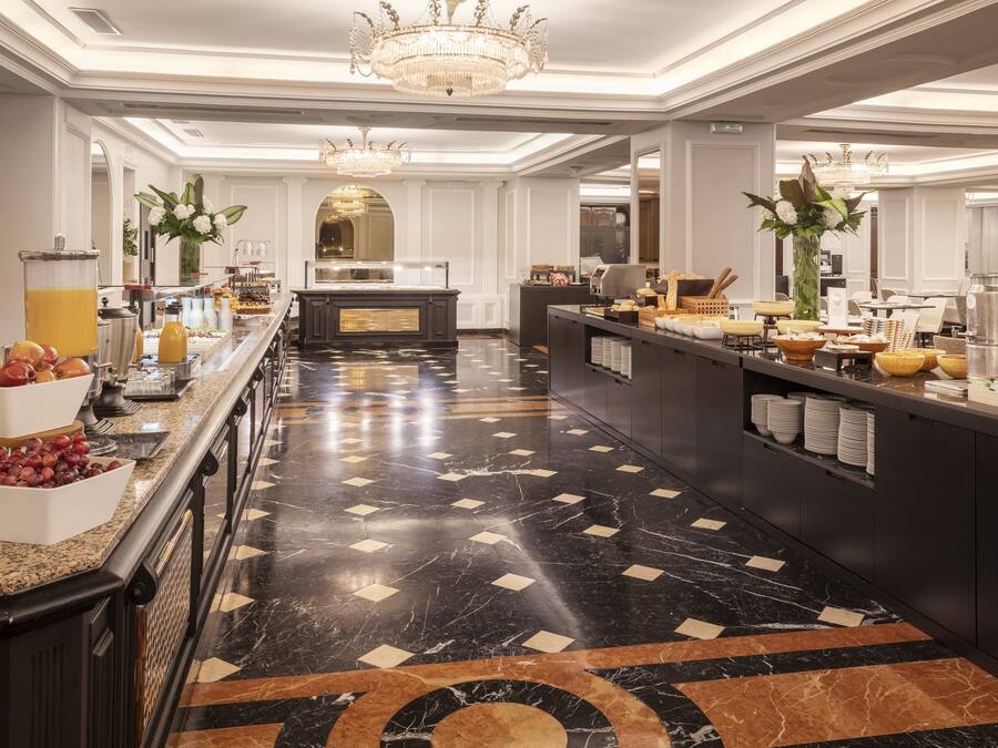 Un hall de hotel espacioso con suelo de mármol, una recepción central y una zona de bufé con diferentes alimentos y bebidas.