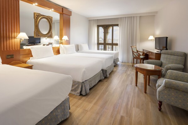 Quarto de hotel com duas camas, uma mesa de escritório com televisão, uma cadeira e uma janela grande com cortinas.