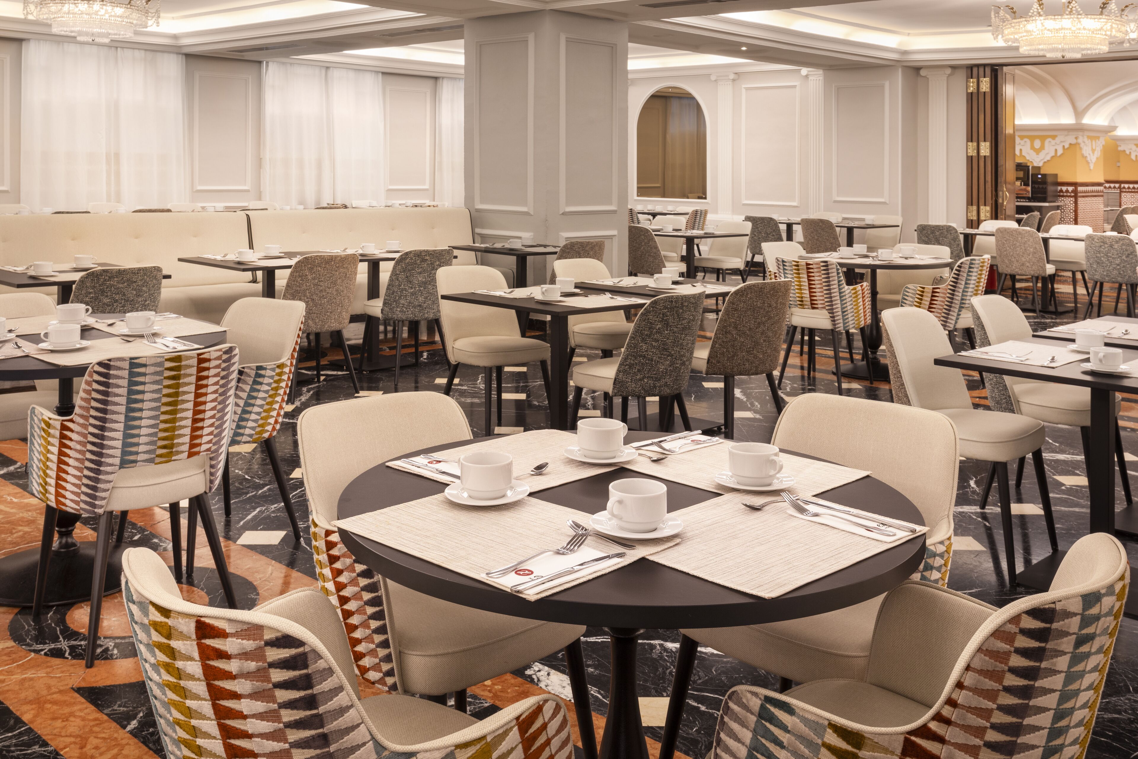 A hotel dining area with multiple tables and chairs, arranged in a spacious layout.