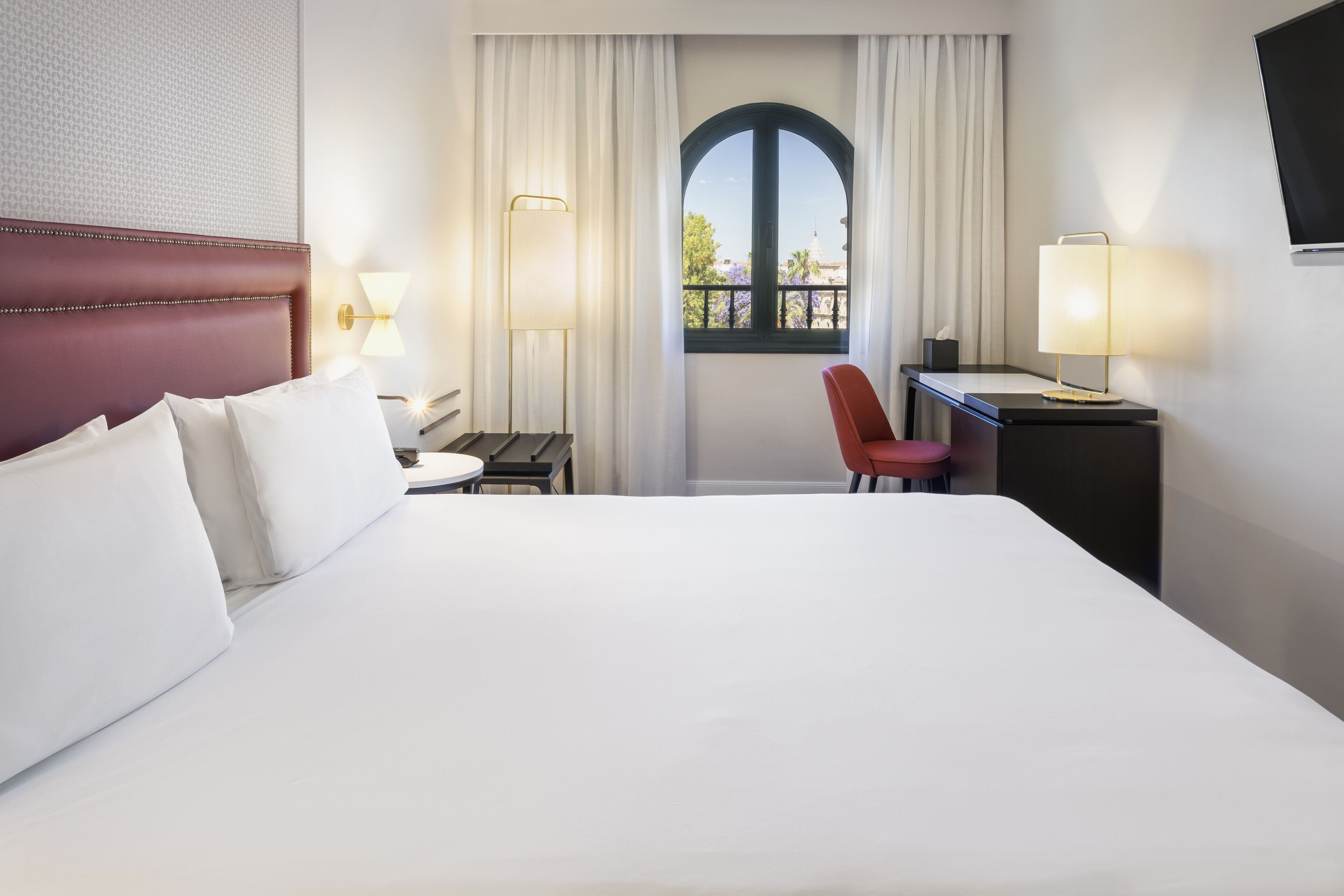 A hotel room with a large bed, a desk, a chair, and a window with a view.