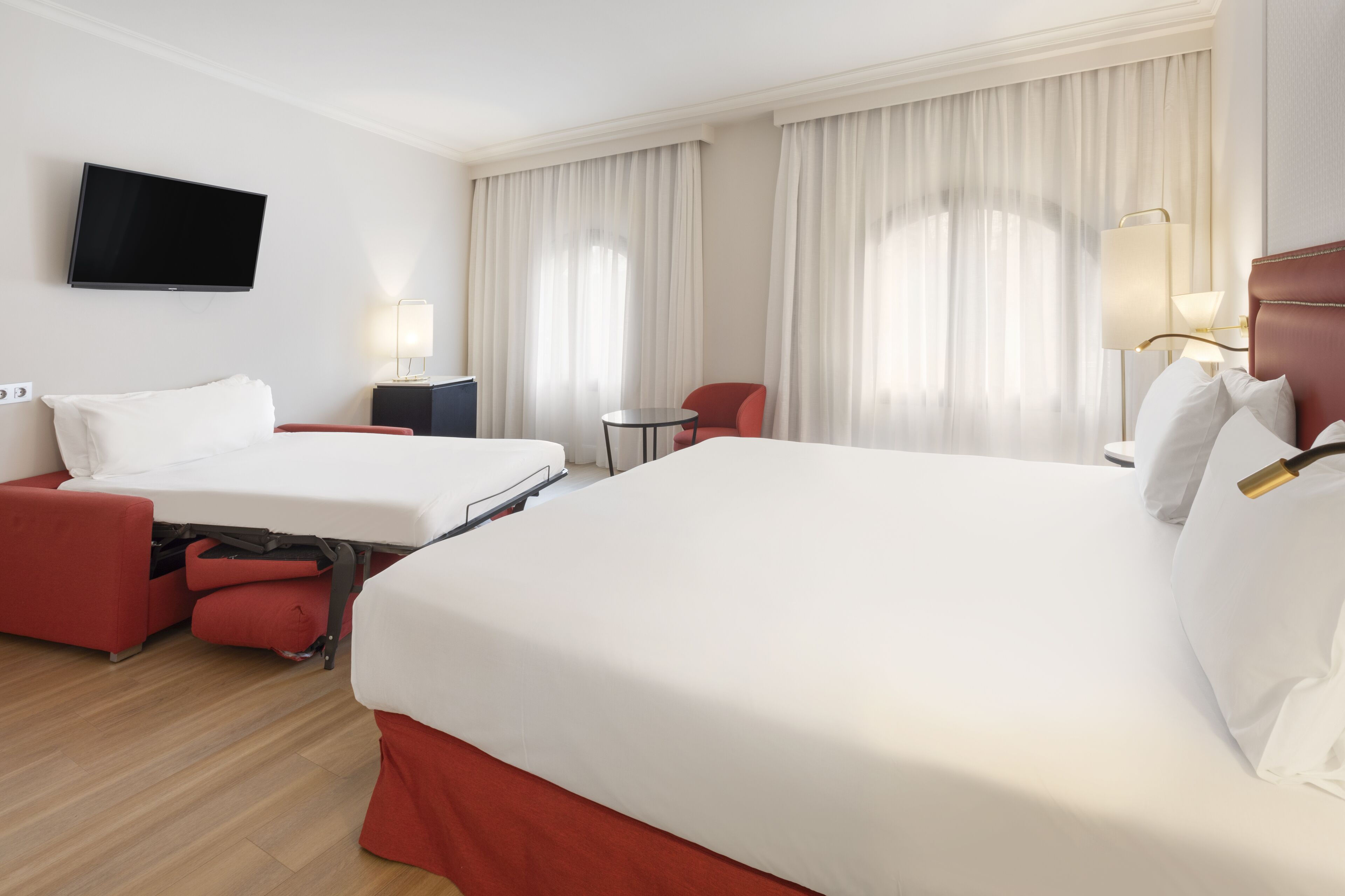 A hotel room with two beds, a TV, a desk, and a chair.