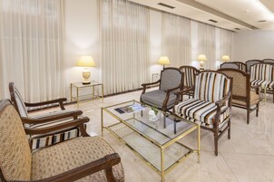 Habitación de hotel con zona de estar que incluye sillas tapizadas a rayas, una mesa de centro de vidrio y dos lámparas sobre mesitas.