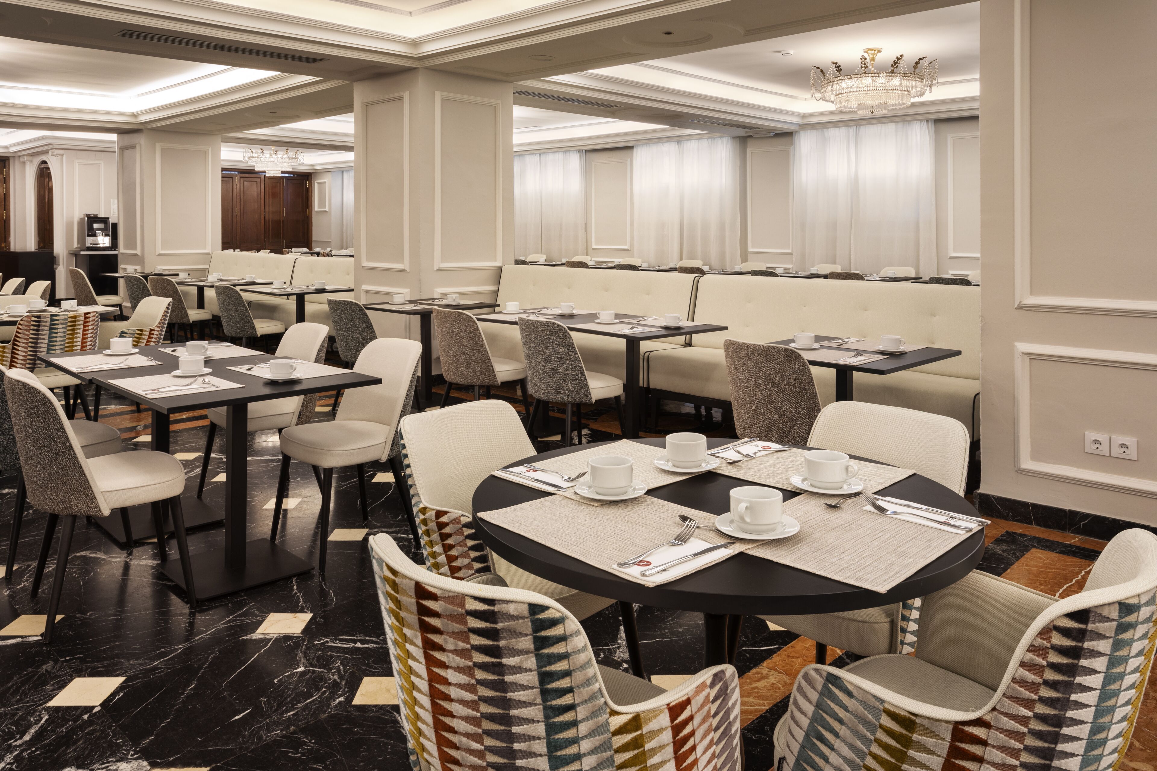 Una sala de dinar d'hotel amb diverses taules i cadires, una làmpada de cristall i una decoració d'interior moderna.